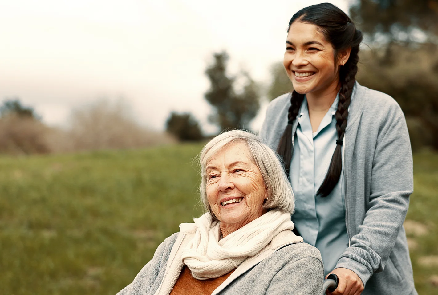 Caregiver pushing a senior woman in a wheelchair outdoors with a smile